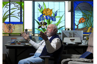 Stained glass artist Tom Randall sits at his work bench at home in the Ellsworth House apartments on Mercer Island