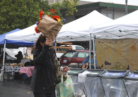 A woman uses a bouquet of flowers to shield her face  from the rain  during the Mercer Island Farmers Market on Sunday