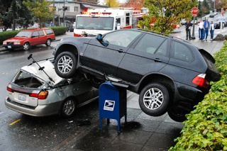A BMW sport utility vehicle rests atop a US Postal Service mailbox and a parked Subaru after jumping a retaining wall out of a parking lot along 76th Avenue SE in the downtown business disstrict on Mercer Island