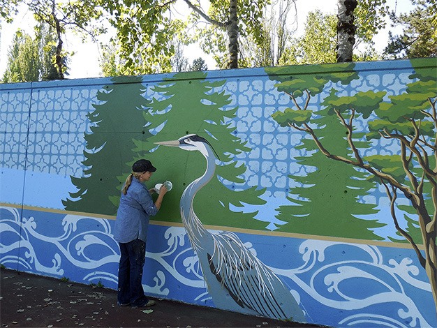Artist Natalie Oswald puts the finishing touches on a graceful blue heron on the new 120-foot-long mural she has designed for the west wall of the tennis courts at Luther Burbank Park.