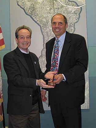 Outgoing mayor Jim Pearman presents the gavel to new mayor Bruce Bassett at the City Council meeting on Jan. 3. Bassett is the 16th mayor since the city incorporated in its present form