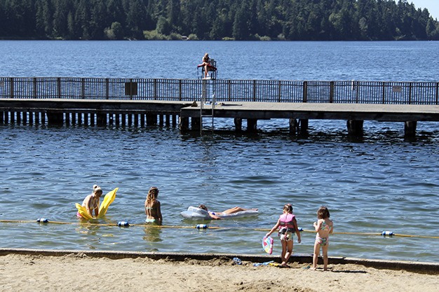 Children play in the sand and water at Groveland Beach in late July as a lifeguard watches from the dock in Lake Washington.