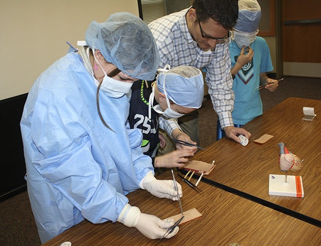 Dr. Michael McMullan of Seattle Children's Hospital has a 'sewing' contest with St. Monica sixth-grader Ryleigh Iverson and fifth-graders Grant Loyd (center) and Alexander Raffetto.