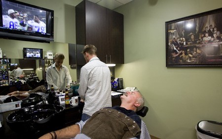 Mercer Island resident Martin Coles watches football while enjoying a straight-razor shave in The Den by barber Nathaniel Landis.