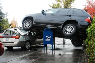A BMW sport utility vehicle rests atop a U.S. Postal Service mailbox and a parked Subaru after jumping a retaining wall out of a parking lot along 76th Avenue S.E. shortly before 3 p.m. in the downtown business district of Mercer Island on Friday.