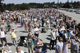 Viewers stand on the closed westbound lanes of the I-90 bridge