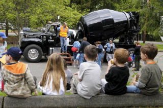 Children sit on the curb while enjoying a snack and watching a 1966 Mack B-61 concrete mixing truck from Glacier Northwest during a truck exhibition day at the Mercer Island Jewish Community Center on Thursday.