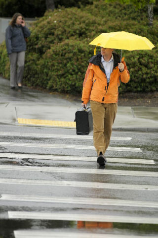 Pedestrians walk across North Mercer Way through spring rain to the Park and Ride bus stops on Mercer Island