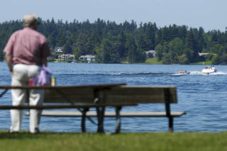 An Islander watches from Luther Burbank Park as two people atop an inflatable raft are towed on Lake Washington.