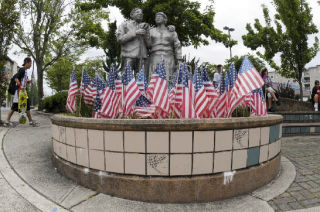 Small flags fill the planter box below the statue of Island pioneers at the corner of 78th Avenue S.E. and S.E. 28th Street at the North end QFC last week.  The day to honor workers was first made a national holiday in 1894..