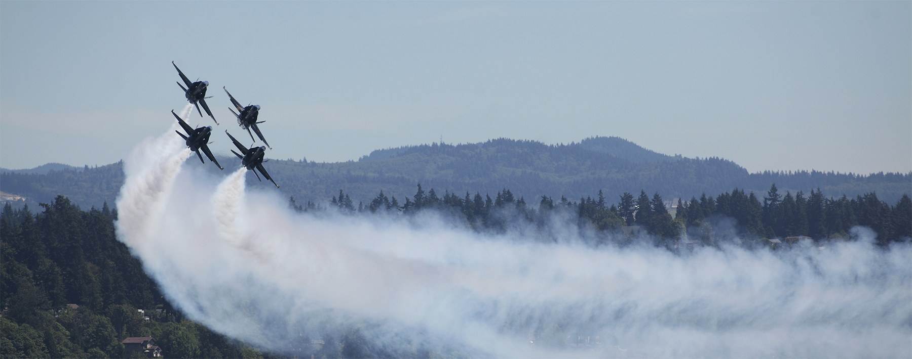Four U..S Navy Blue Angels in diamond formation lay down a trail of smoke as they pass center stage with the crest of Mercer Island visible in the background on July 31
