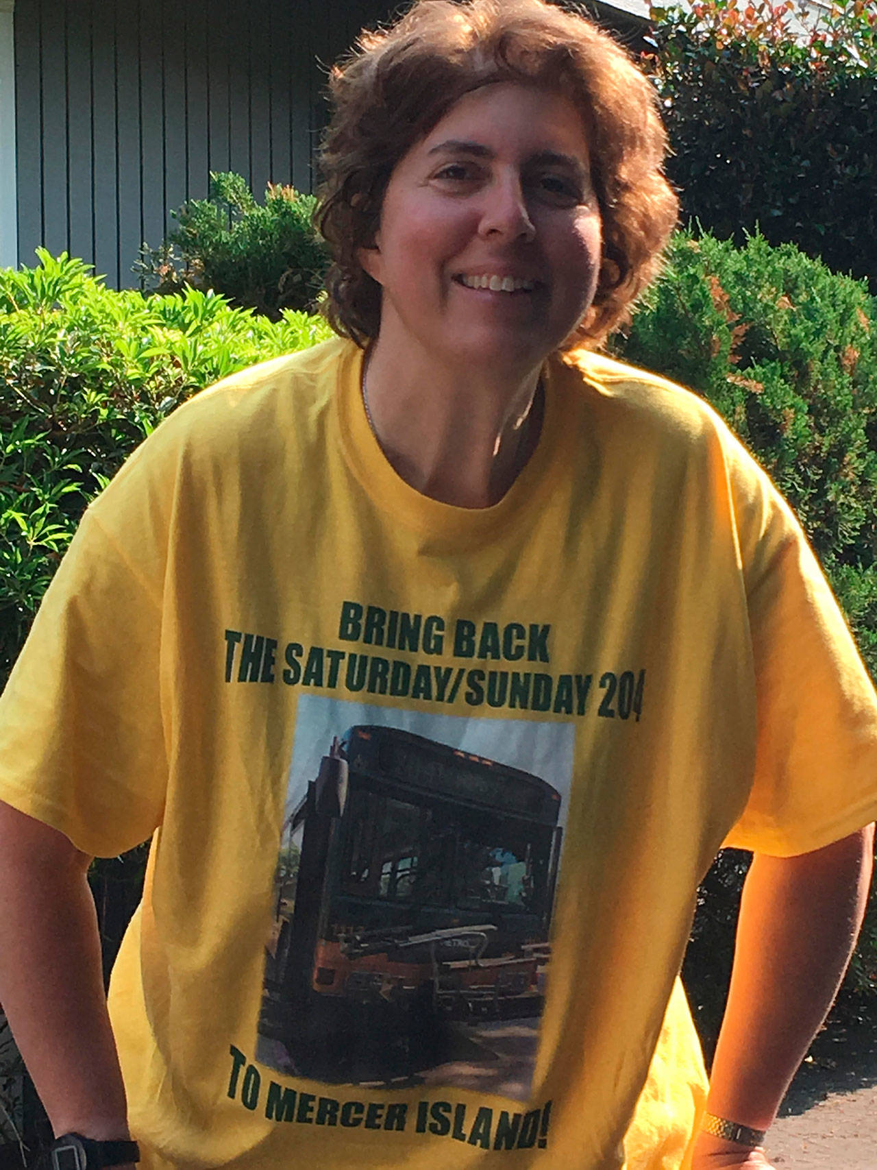 Mercer Islander Vicki Rouillard wearing her T-shirt she designed that states “Bring Back The Saturday/Sunday 204.” The shirt is yellow and green, the same colors as Metro’s buses.