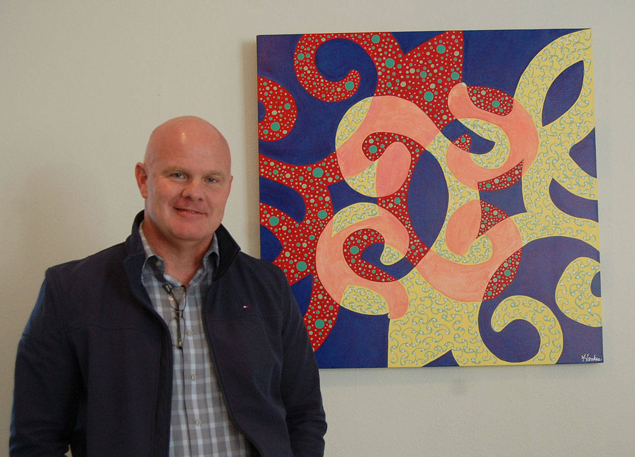 New MICA Executive Director Paul Shoemaker, posing in the MICA office with a painting by Louise Elaine Hankes, wants to reintroduce the arts organization to the community. Katie Metzger/staff photo