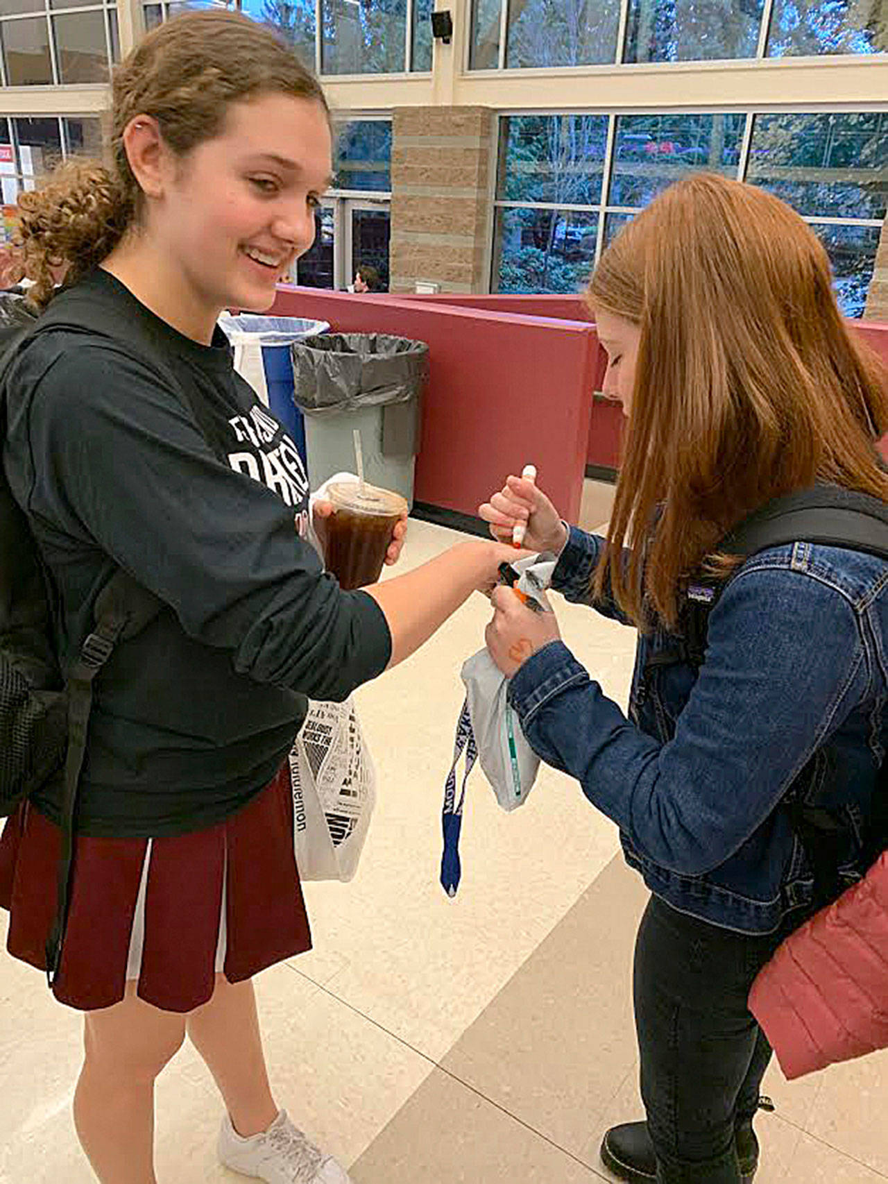 Bella Hartman draws orange hearts on Sophie Gottesman’s hand for her refugee awareness day at MIHS on Nov. 15. Courtesy photo