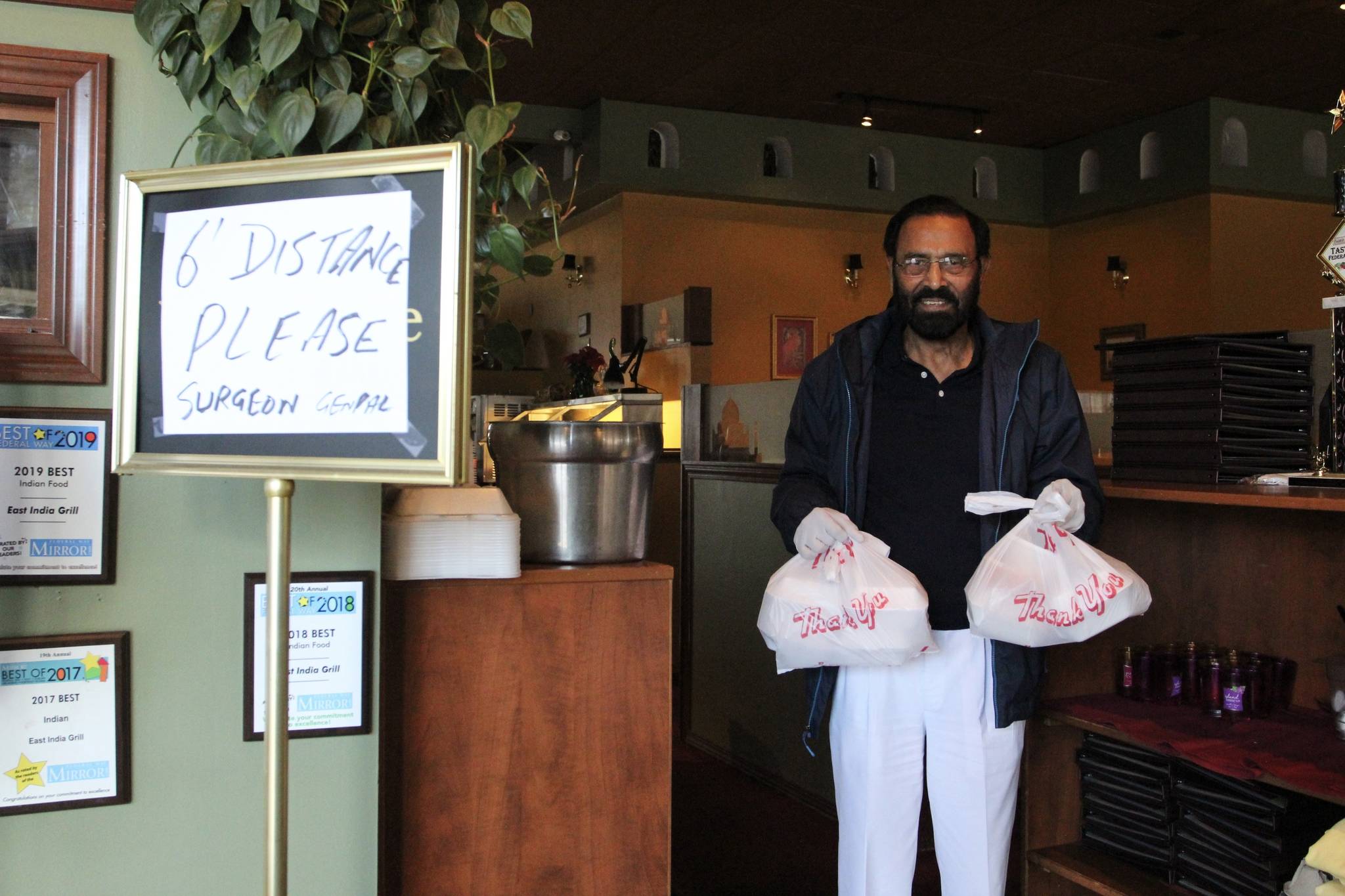 Kabal Gill, owner of East India Grill in Federal Way, wears gloves to hand over take-out orders at his restaurant. File photo
