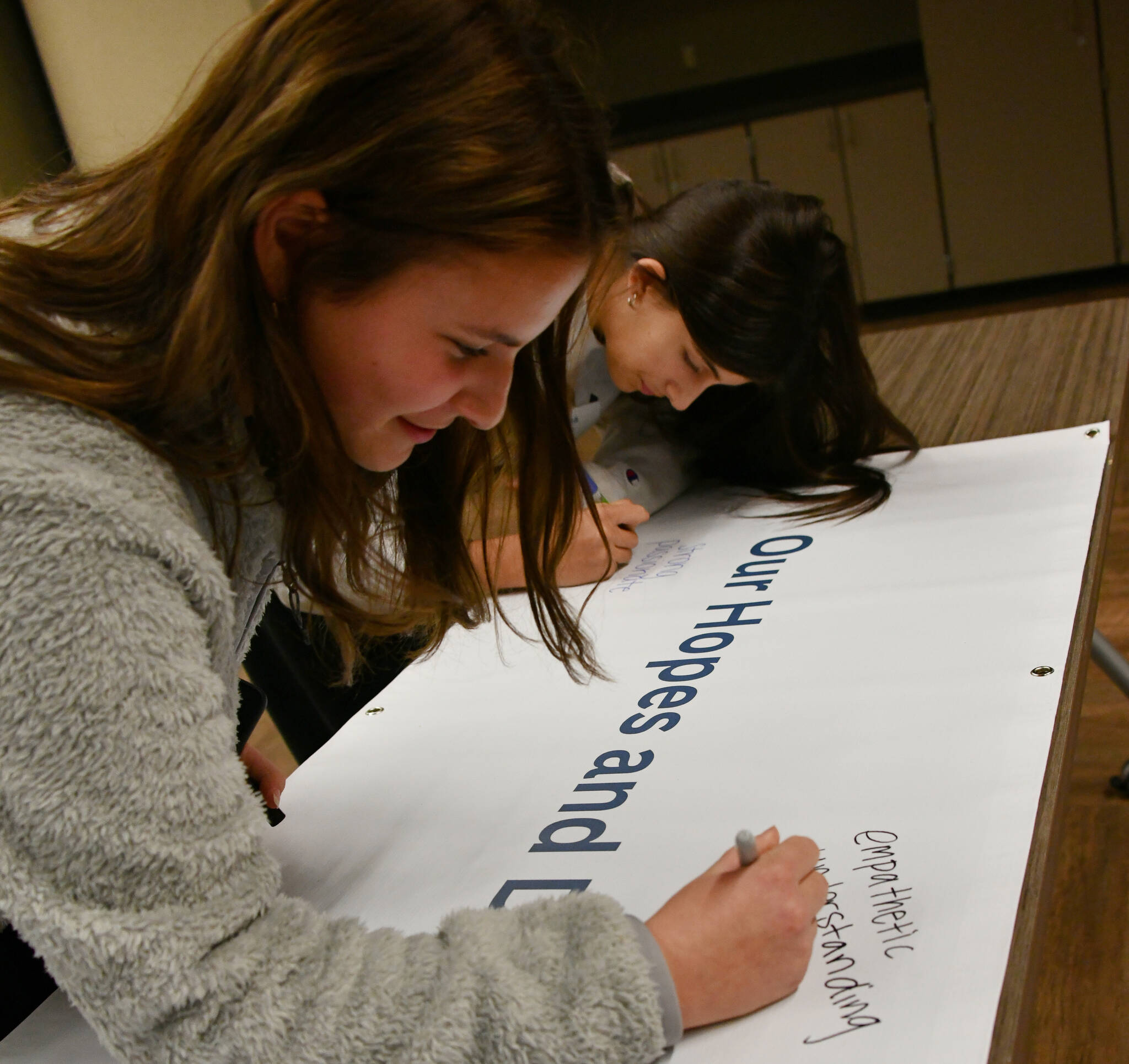 Mercer Island High School freshmen Nadia Slivinski, left, and Anna Mock jot down their thoughts on the “Our Hopes and Dreams for Mercer Island Youth” banner at the MI Healthy Youth Forum 2022. Some of the messages were, “strong, passionate, caring,” “empathetic, understanding, loving” and “responsible, loving, kind.” Andy Nystrom/ staff photo