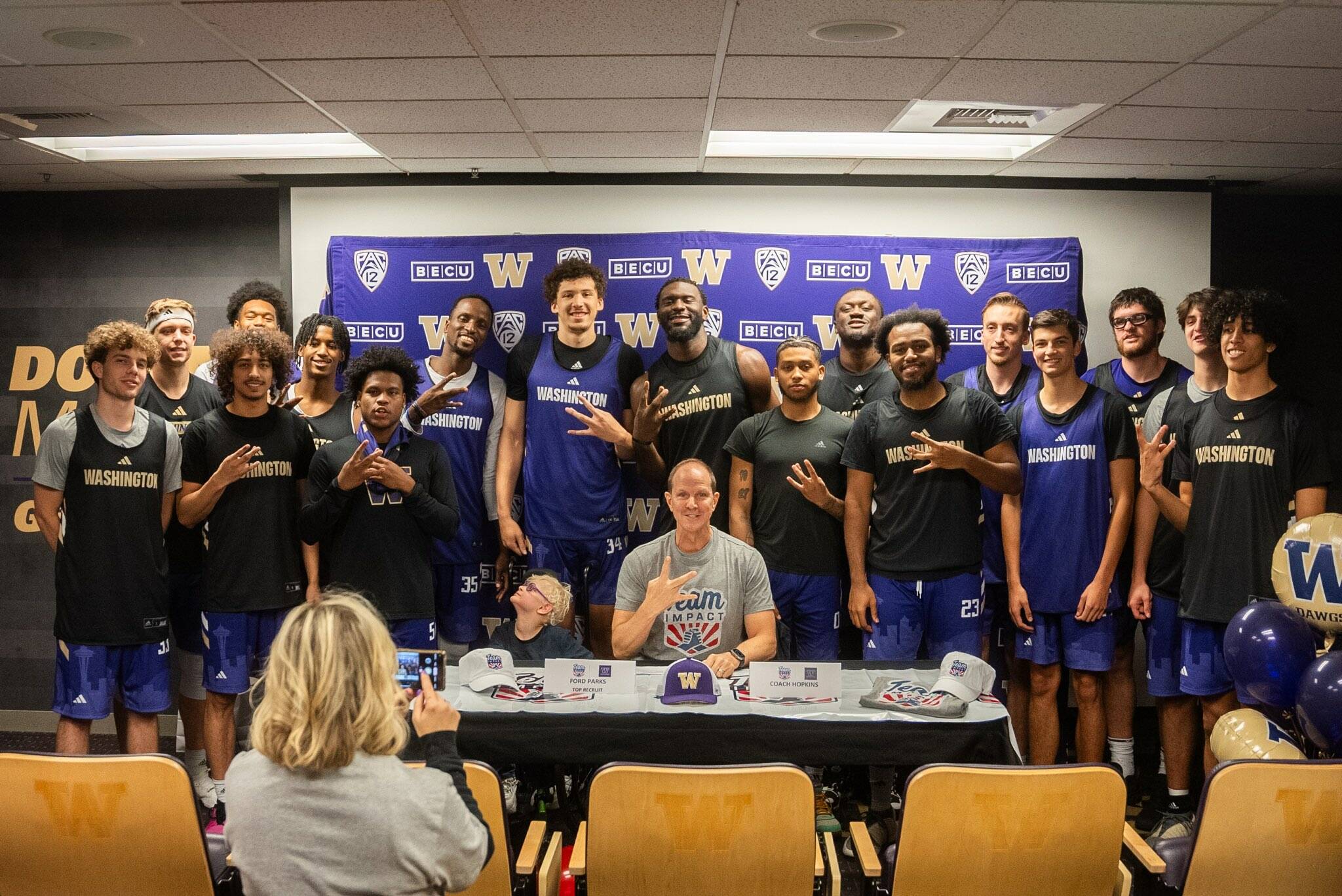 Seven-year-old Ford Parks of Mercer Island poses with the University of Washington men’s basketball team while his mother Effie Parks takes photos. Ford, who is battling a rare genetic disorder, signed with the Huskies through Team IMPACT, a nonprofit organization matching disabled children with college athletic teams across the country. Coach Mike Hopkins described the newest addition to the team as “tough, hardworking and full of joy,” during an emotional ceremony on Oct. 18. Ford will attend team activities, including practices and games, for the next two seasons. He is enrolled at Northwood Elementary School on the Island. Hopkins said: “Our program is built around toughness, grittiness and togetherness. Ford is 7, and he’s already overcome more adversity than most people do their whole lives.” Ford is battling a rare genetic disorder called CTNNB1 Syndrome. Team IMPACT is a Boston-based nonprofit that connects children facing chronic illnesses with college teams. Photo courtesy of UW Athletics