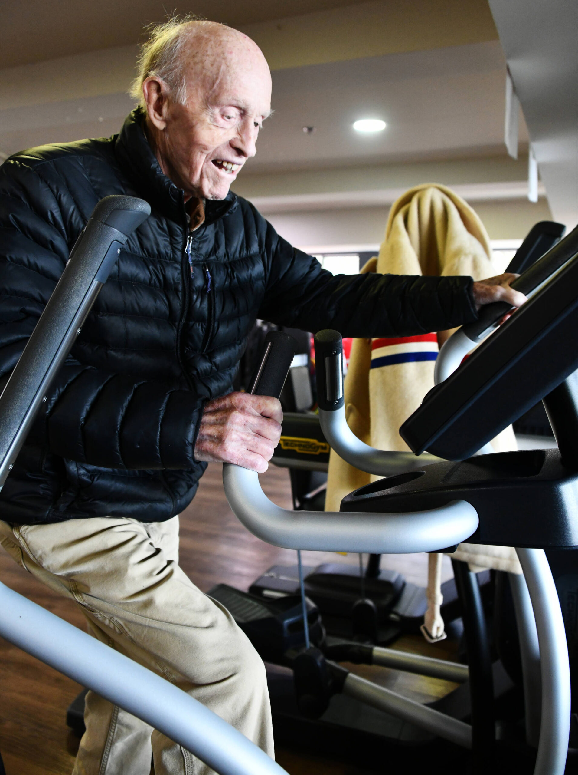 Peter Kennedy powers through an elliptical machine workout at Covenant Living at the Shores on Mercer Island. His 1952 Winter Olympics coat hangs to the side. Andy Nystrom/ staff photo