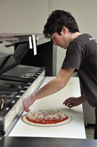 Michel DeBange spreads cheese on top of a pizza at Zaw Pizza.