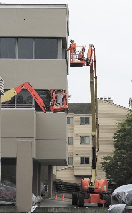 Painters work on the top floor of the Caledonian building in the 3000 block of 80th Ave. S.E. Despite Tuesday's light rain