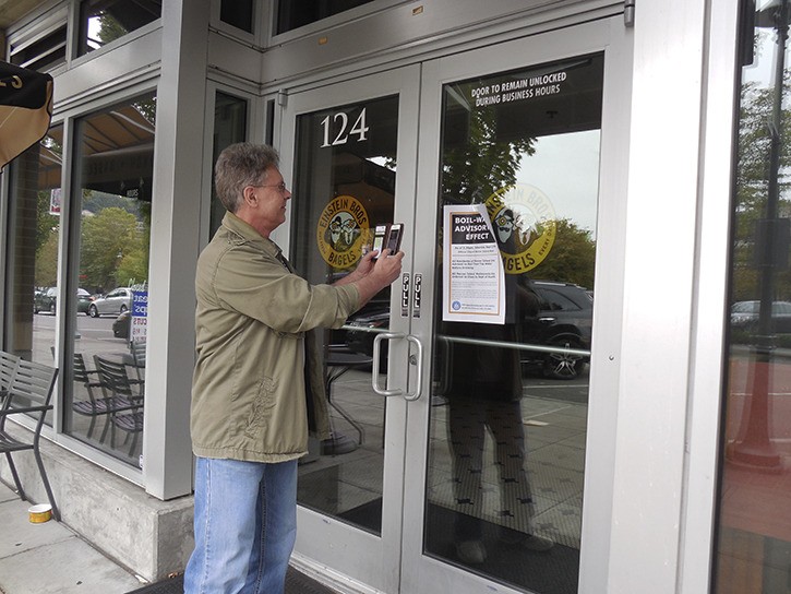 Islander Peter Jurca takes a photo of the boil water notice on the front door of Einstein’s Bagels on Sunday to share with friends in the Philippines. He said they would appreciate the irony of water problems in the United States. The boil water advisory was lifted Monday morning.