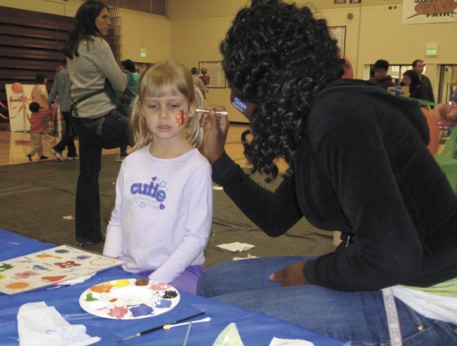 Mercer Island High School student Queen Opoku paints a butterfly on preschooler Kayla Gross during the annual Mercer Island Preschool Association's Circus.