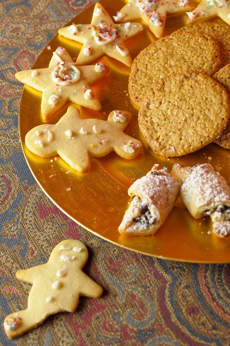 Chocolate rugelach for Hanukkah is made with rich pastry dough wrapped around chocolate chips fills a plate with frosted and decorated butter cookies for Christmas. Benne cakes for Kwanzaa are made with brown sugar and sesame seeds.