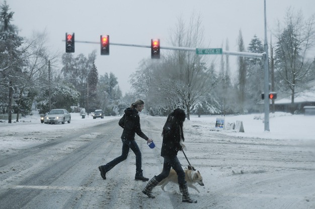 Pedestrians walk through the intersection of S.E. 40th Street and Island Crest Way through the snow.