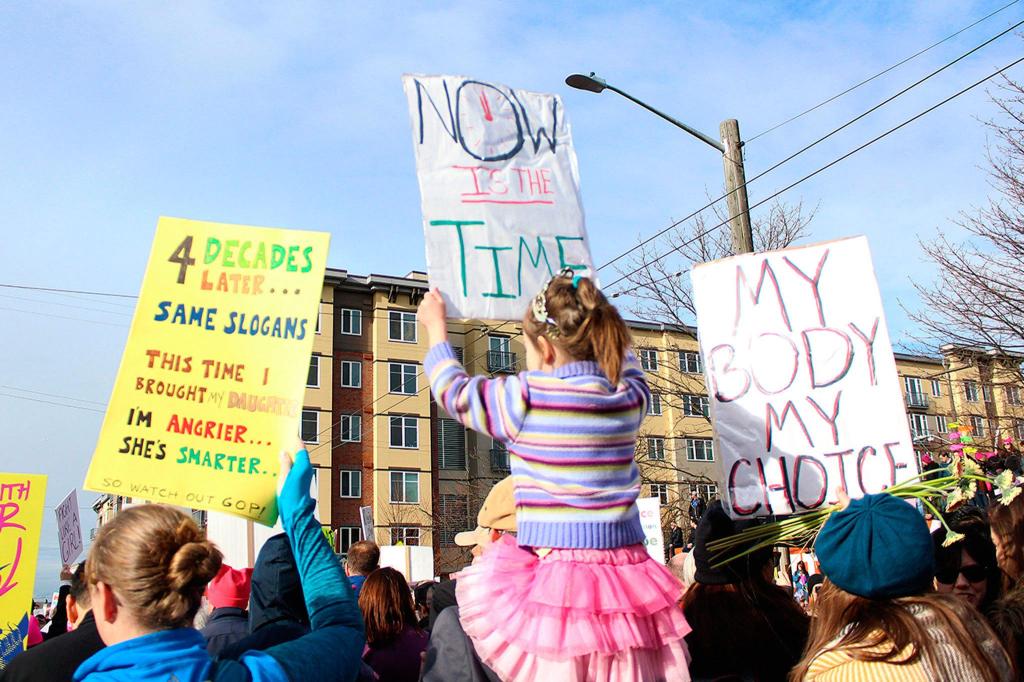 Marchers hold up signs as they walk to Seattle Center. Allison DeAngelis/Bellevue Reporter