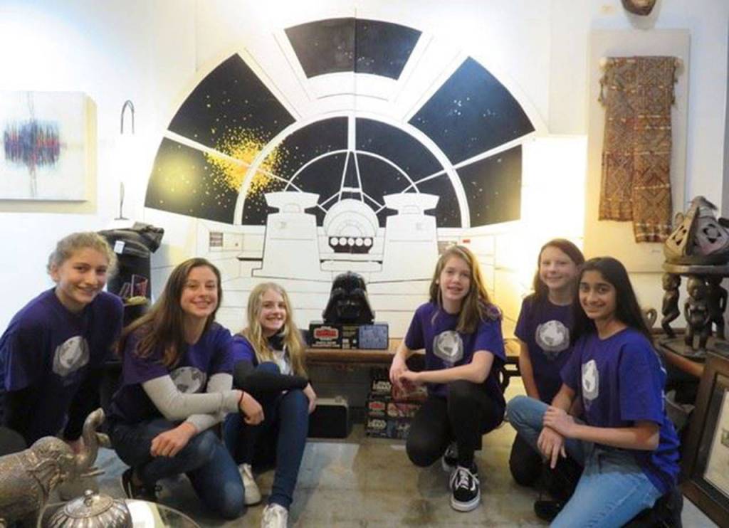 Middle school students and MIYFS volunteers pose in front of the Millennium Falcon mural at Clarke and Clarke Art and Artifacts, which is participating in the Shop and Dine Local event on Feb. 7-8. The mural will be auctioned in February, with a portion of the proceeds going to the MIYFS Foundation. Photo courtesy of MIYFS Foundation