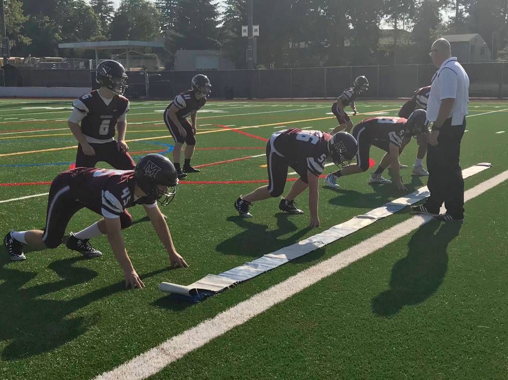 The Mercer Island front seven (linebackers and defensive line) get into their stances while the coaching staff delivers signals and line calls. Shaun Scott/staff photo