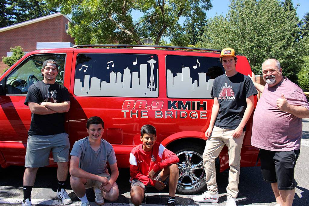 Madison Miller / staff photo                                KMIH 88.9 The Bridges radio station general manager, Joe Bryant (right) stands with four of his students working on the Log Boom Radio Seafair broadcast in front of the stations new (used) van. From left: Max Tanzer, Gabe Gottesman, Sam Shroff, Mason Meinzinger and Joe Bryant.