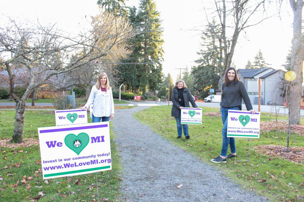 From left, Mercer Island Community Fund grant chair Debbie Hanson, treasurer Betsy OConnell and president Erin Krawiec stand with We Love Mercer Island signs that are staked all over the Island. Natalie DeFord/staff photo.