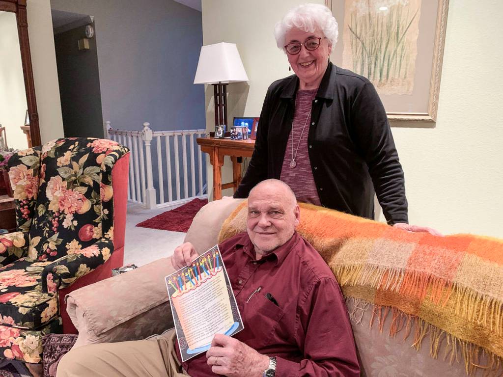 In their Mercer Island home, Pat and Dan Braman pose with a flier asking friends and family to plant 80 trees for their 80th birthdays and to help the environment. Natalie DeFord/staff photo