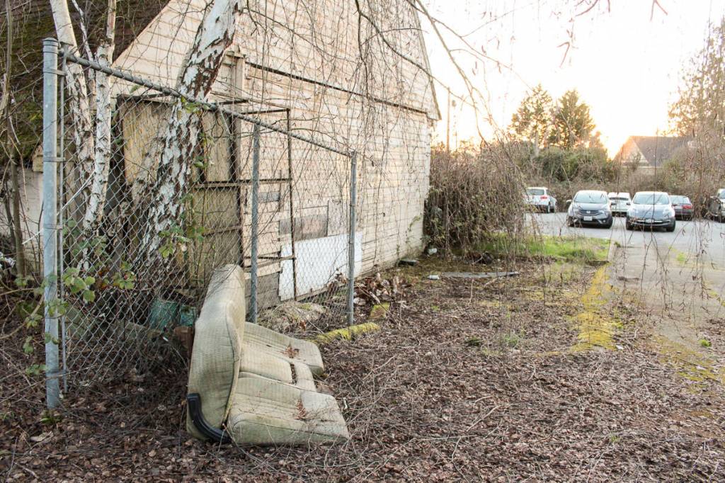 The old East Seattle Elementary School building boarded up and surrounded by various discarded items and trash.