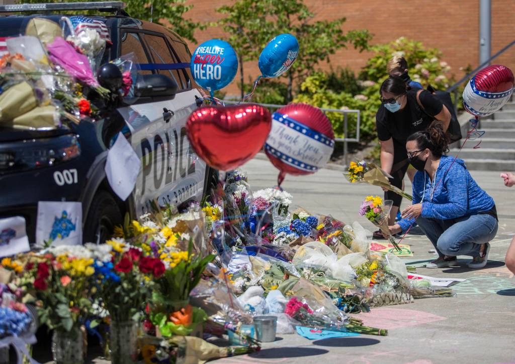 People place flowers at a memorial Tuesday in front of Bothell City Hall for a Bothell police officer who was killed Monday night. (Olivia Vanni / The Herald)