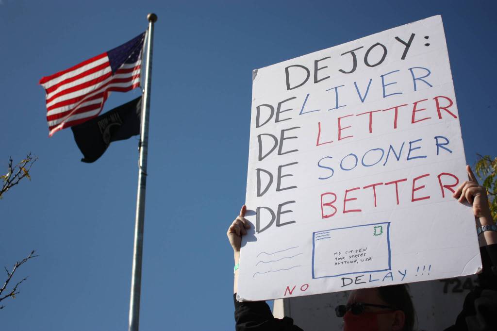 Postal worker hold sign criticizing Postmaster Louis DeJoy (photo credit: Cameron Sheppard)