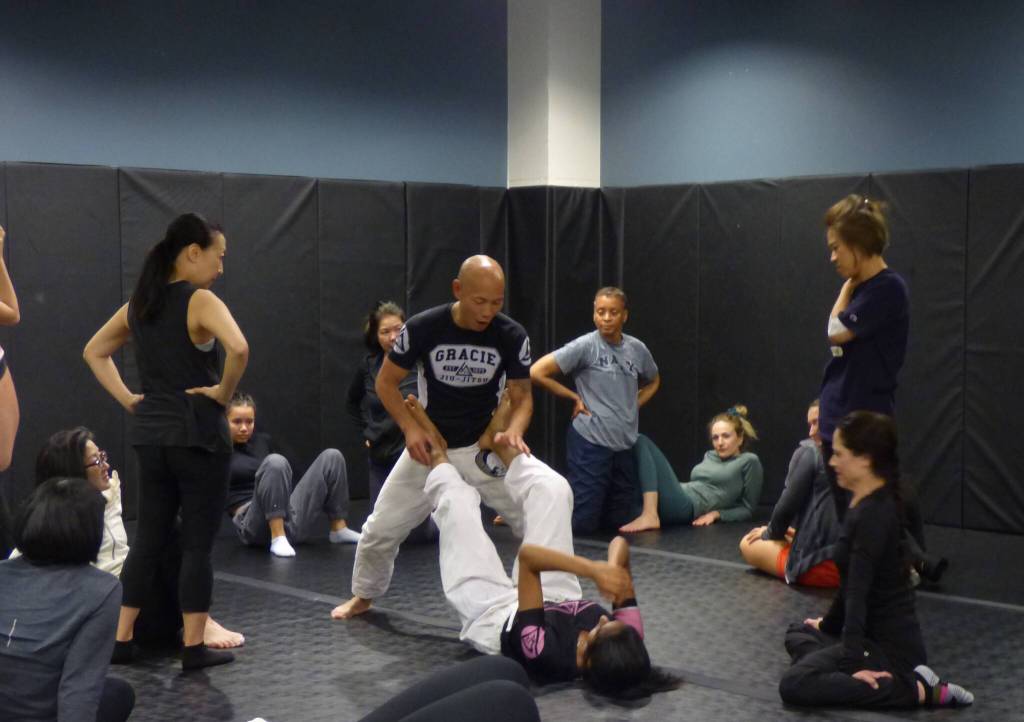 Hanaumi and a volunteer show participants how to defend on the ground before they break out to practice in pairs. (Cameron Sires/ Sound Publishing)