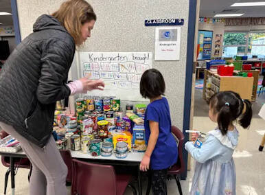 West Mercer kindergarten teacher Tara Hutschreider helps two of her students add tally marks to the sheet tracking student food donations. Photo courtesy of the Mercer Island School District