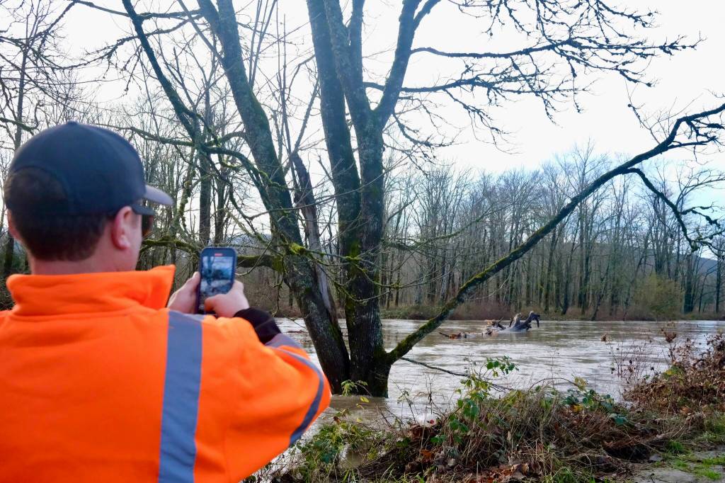 King County Flood Patrol member Seth Ballhorn photographs a tree as it floats down the Snoqualmie River during flooding Dec. 9, 2025. (Grace Gorenflo/Sound Publishing)